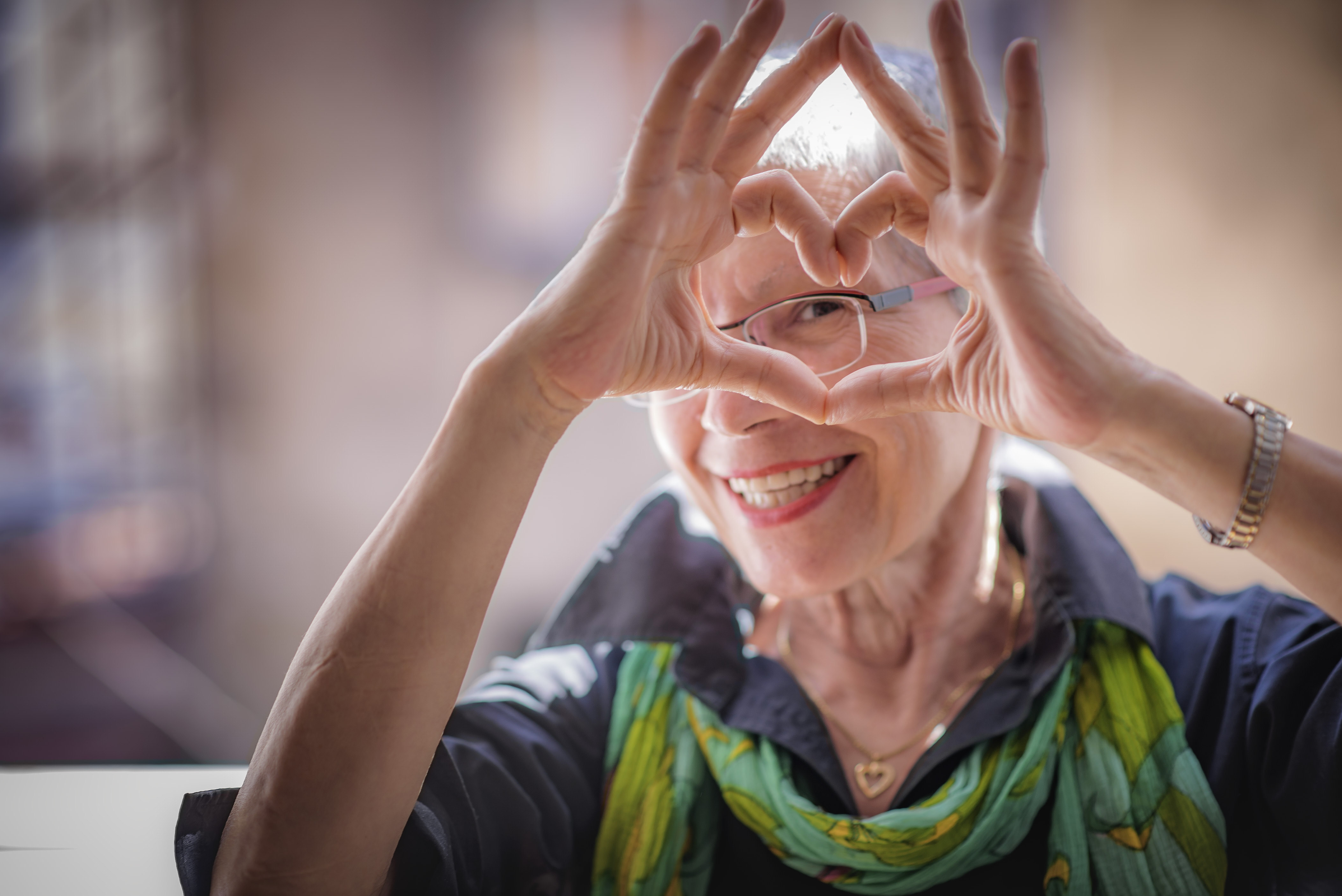 A woman making a heart shape with her hands in front of her face, you can see her eye through the heart shape.