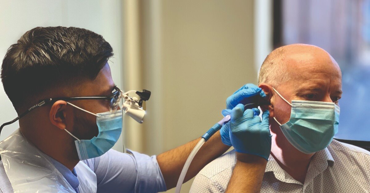 A man conducts a hearing test on an elderly man, both are wearing face masks.
