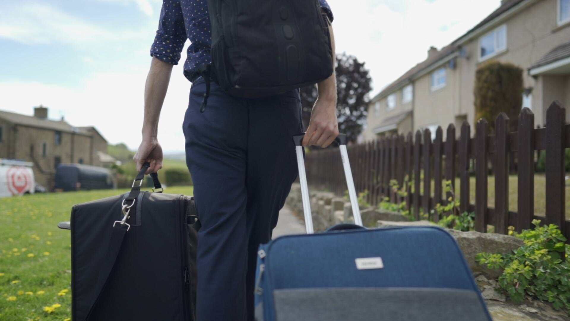 A person walking down a residential street holding two suitcases.