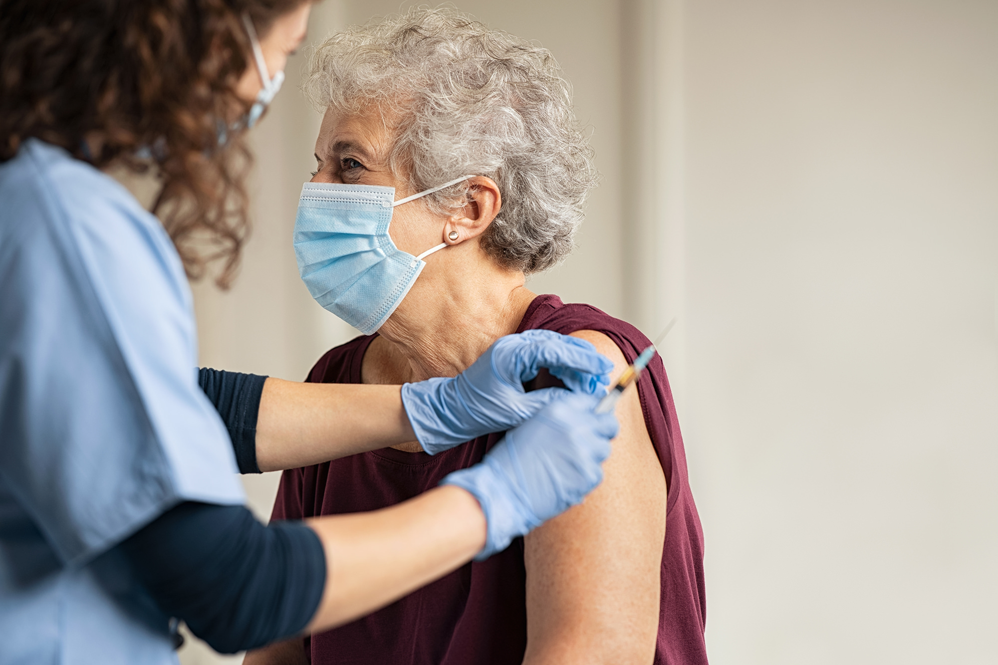 An elderly woman receiving a vaccination from a nurse. Both are wearing face masks.