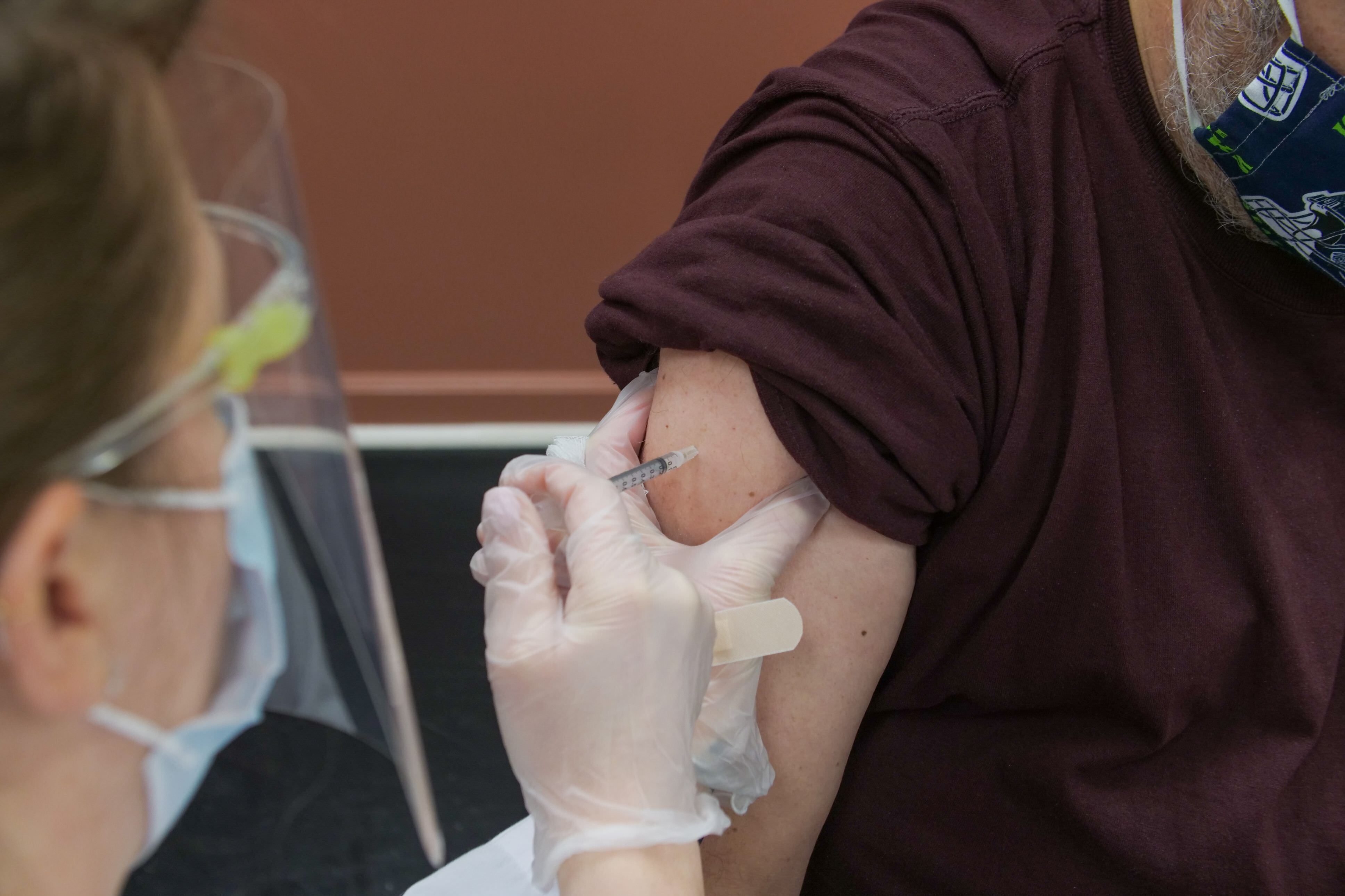 A person receiving a vaccination from a nurse in a face mask.