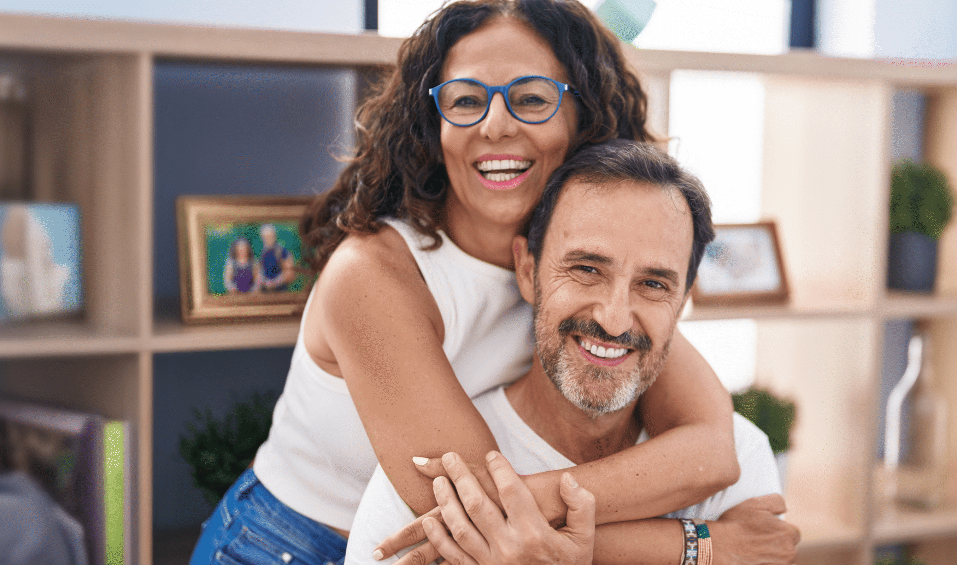 A woman embraces a man from behind in a living room.